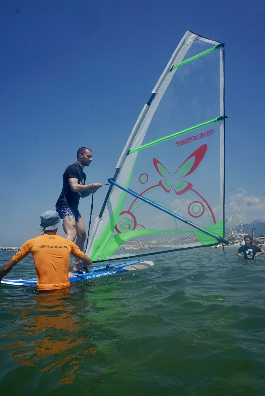 Allievo sulla tavola a vela seguito da un istruttore WE RIDE in acqua